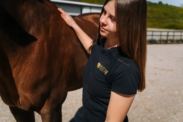 Călăreață zâmbind în timp ce își mângâie calul, la Elite Riders Academy
